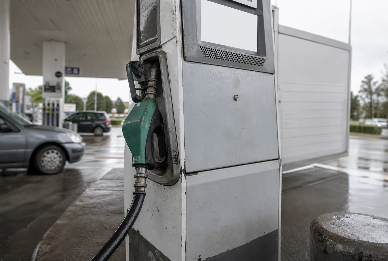 Pompe à carburant humide en bord de route, gros plan sur le pistolet et le flexible, station-service sous la pluie.