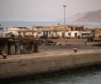 Quais en béton du port de Mokha, bollards usés, embarcations de travail et bâtiments bas face à la mer Rouge.