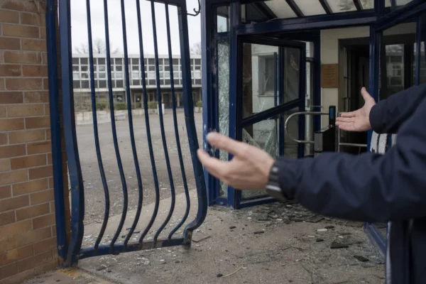Portail et sas d’entrée d’un lycée endommagés après des dégradations, avec des débris au sol.