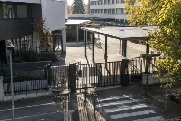 Portail métallique et grilles à l’entrée d’un lycée, avec les bâtiments scolaires visibles derrière la clôture.