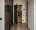 Porte d’appartement entrouverte dans un hall résidentiel, couloir vide avec boîtes aux lettres et traces d’usage.