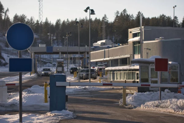 Poste frontière routier en France, barrière levée, véhicules en attente et bâtiment de contrôle sous un soleil d’hiver.