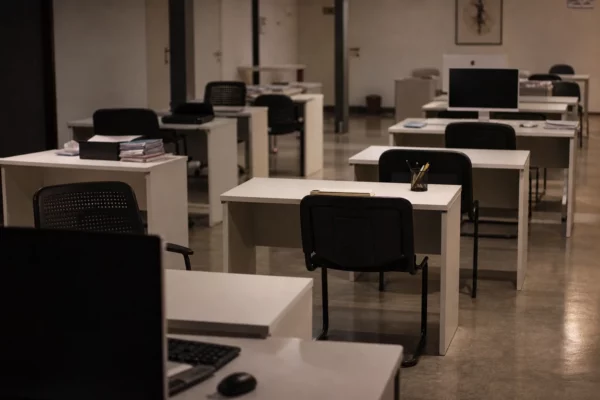 Bureau d’administration publique presque vide, écrans éteints et postes de travail désertés sous lumière chaude du soir.