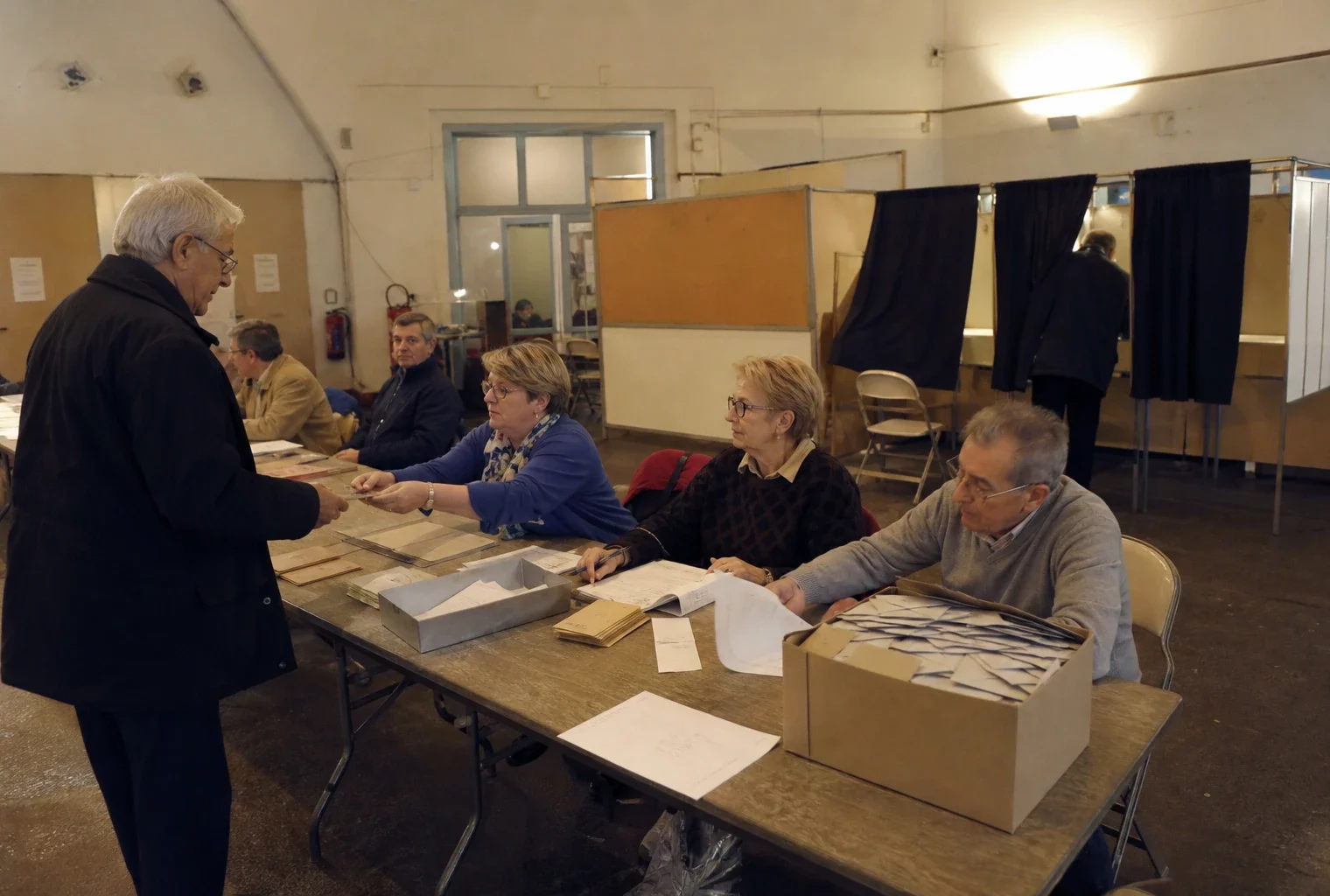 Salle de vote d’une primaire politique avec tables d’émargement, isoloirs et bulletins prêts pour le dépouillement.