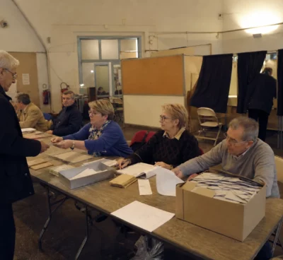 Salle de vote d’une primaire politique avec tables d’émargement, isoloirs et bulletins prêts pour le dépouillement.