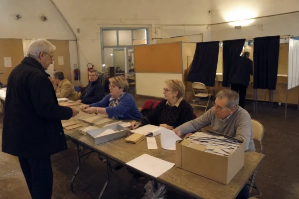 Salle de vote d’une primaire politique avec tables d’émargement, isoloirs et bulletins prêts pour le dépouillement.