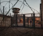 Vue d’une prison algérienne derrière des barbelés, avec portail, murs d’enceinte et bâtiments de détention en arrière-plan.