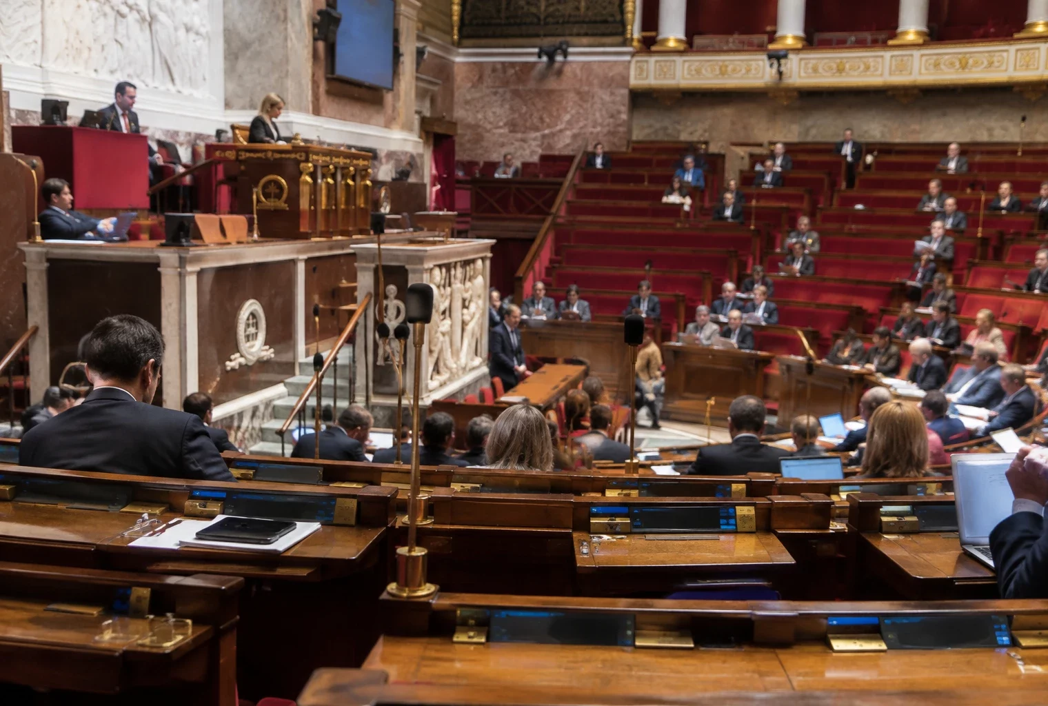 Rangées de pupitres parlementaires équipés de microphones et de dispositifs de vote dans une salle de séance.