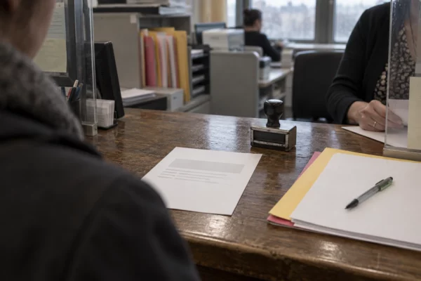 Un récépissé administratif vierge et un tampon sur un comptoir de préfecture, avec des dossiers rangés derrière le guichet.