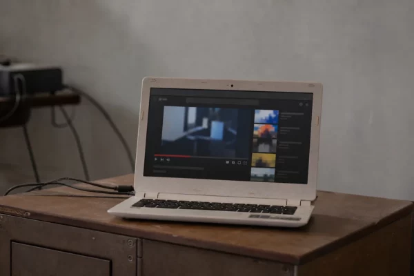 Ordinateur portable ouvert sur une plateforme vidéo, posé sur un bureau simple avec câbles et mur neutre en arrière-plan.