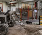 Robot de prospection lunaire en test dans un atelier spatial français, sur sol technique avec câbles et structures industrielles.