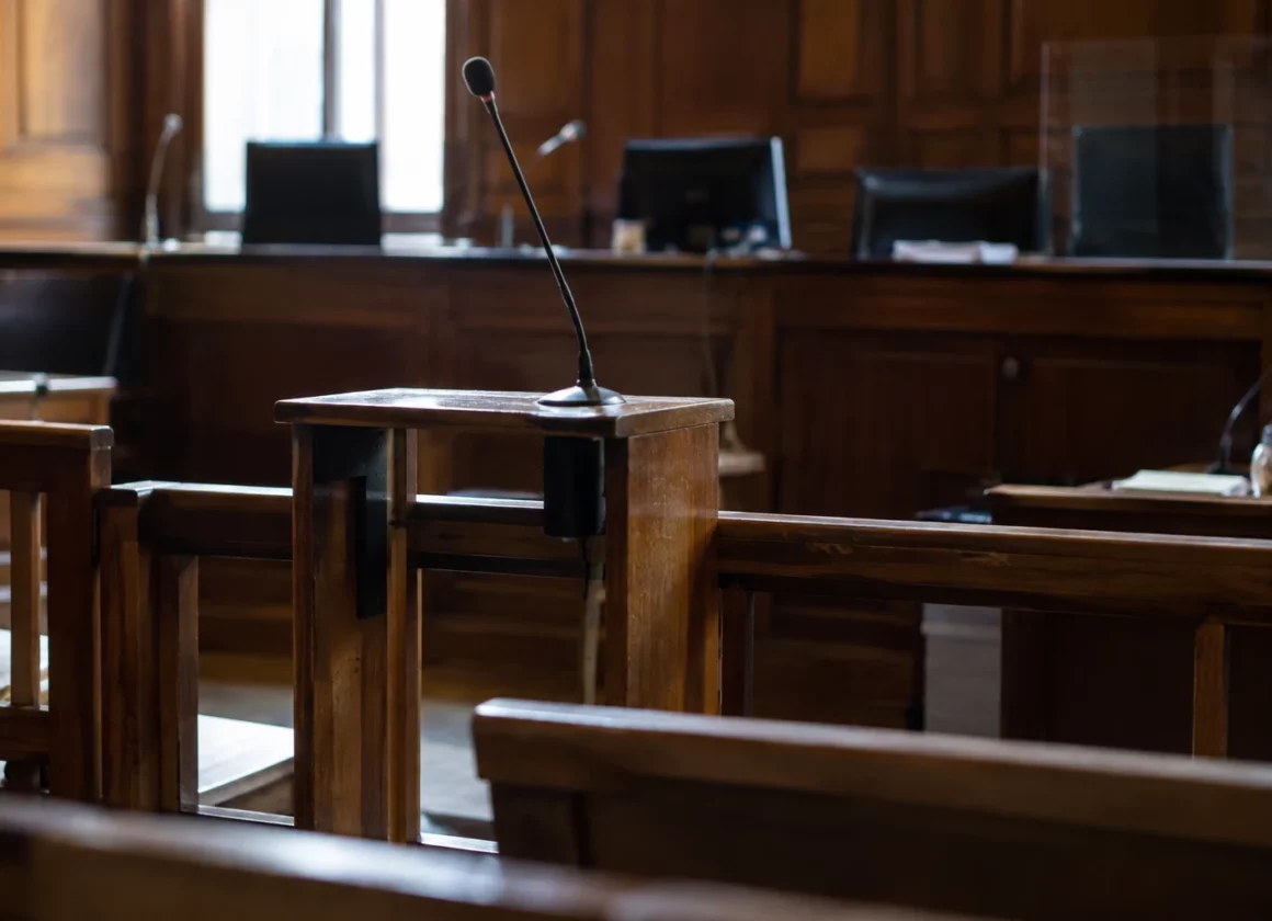 Salle d’audience correctionnelle avec bancs, barre et pupitres équipés de microphones, sans personne présente.