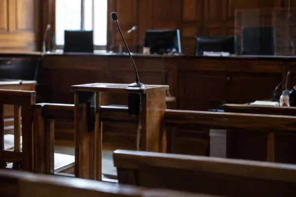 Salle d’audience correctionnelle avec bancs, barre et pupitres équipés de microphones, sans personne présente.