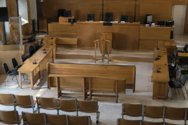 Salle d’audience vide avec le banc des prévenus, les places des avocats et l’estrade de la juridiction au fond.
