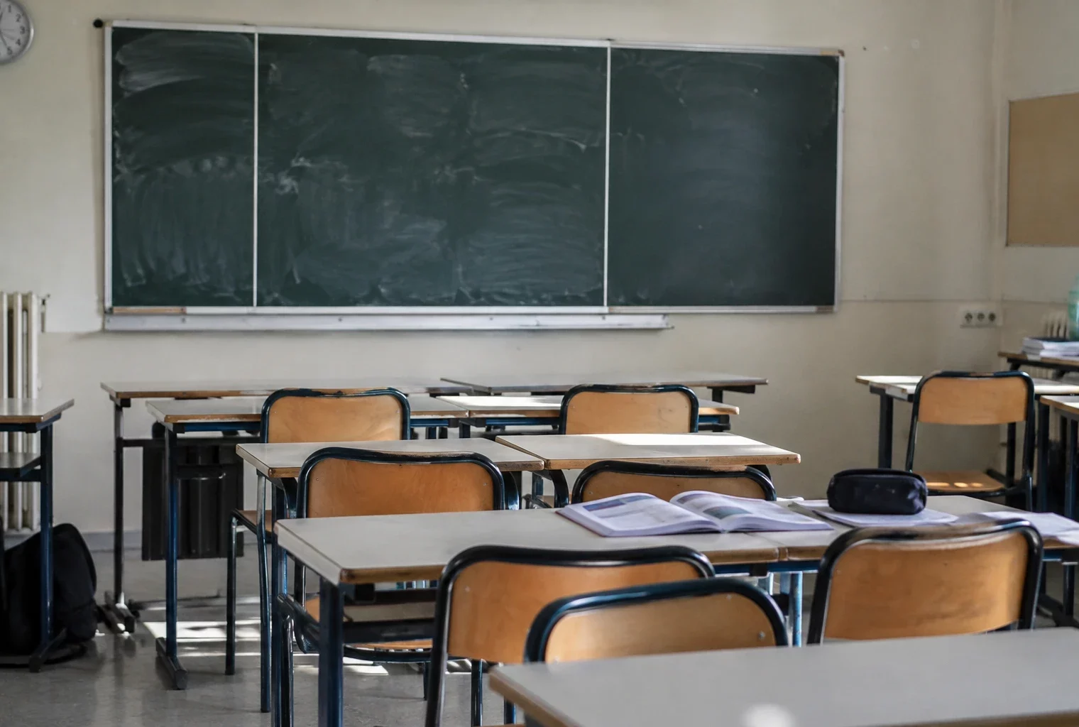 Salle de classe vide avec des tables d’élèves, des chaises et un tableau mural, sans inscription lisible ni personne.