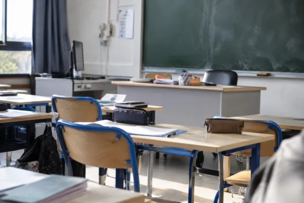 Salle de classe de lycée avec des tables d’élèves en rangées, des chaises et un tableau mural au fond.