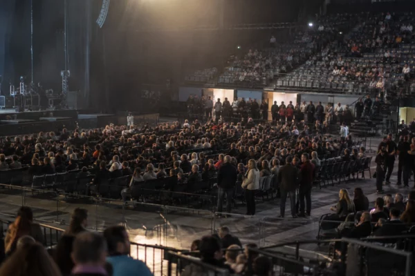 Rangées de sièges occupées dans une salle de spectacle, avec des personnes debout près d’une allée d’accès.