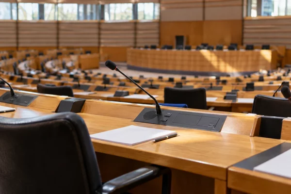 Détail d’un pupitre en bois et de son microphone dans une salle de conseil municipal aux sièges disposés en rangées.
