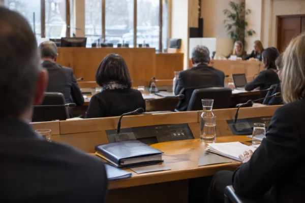 Pupitres équipés de microphones et dossiers fermés dans une salle de conseil municipal, sans élus présents.