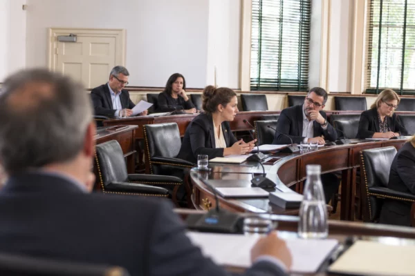 Dans une salle de conseil aux bureaux de bois usés, des élus délibèrent autour de dossiers et de microphones.