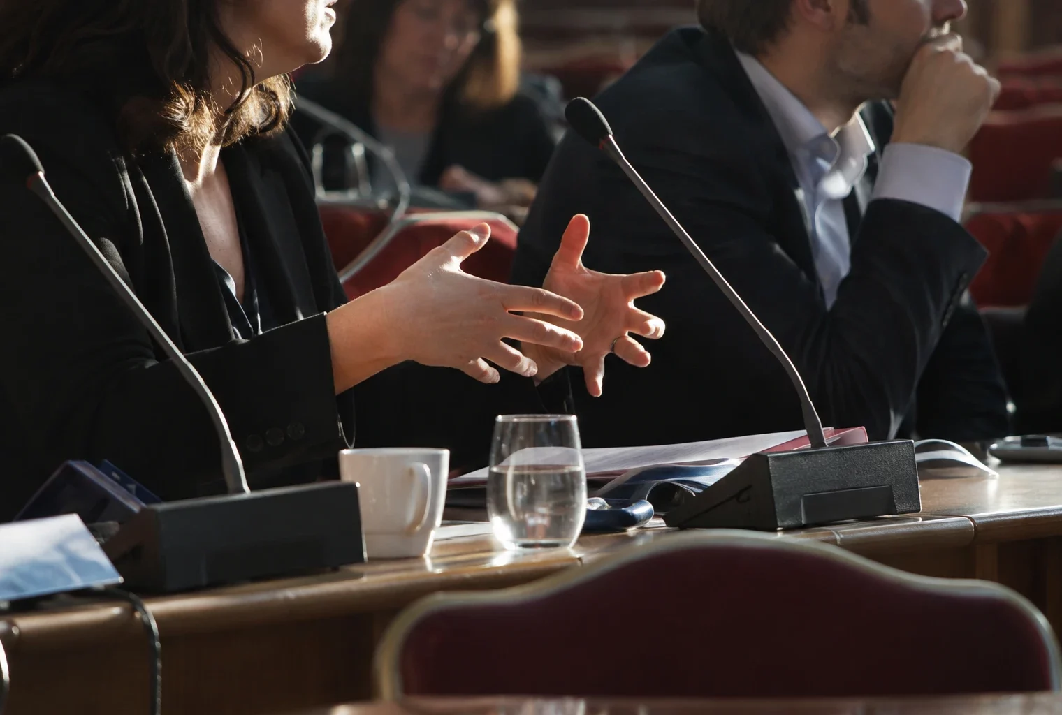 Pupitres équipés de microphones et sièges disposés dans une salle de réunion politique, sans inscription ni logo visible.