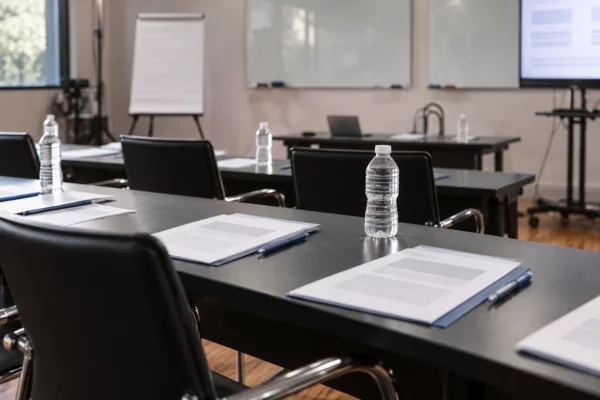 Dossiers et feuilles de travail vierges sur une table devant des chaises alignées dans une salle préparée pour une formation syndicale.