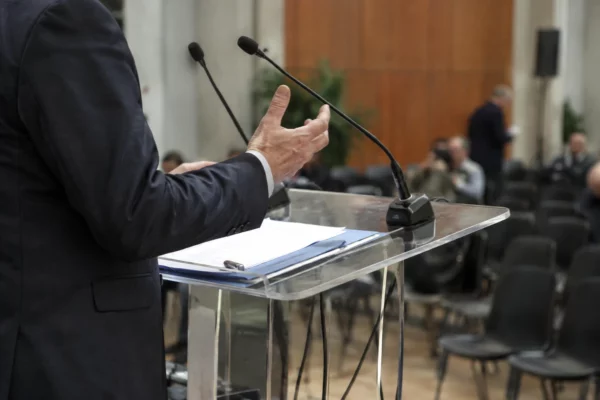 Pupitre équipé de micros dans une salle polyvalente aménagée pour un meeting politique, devant des rangées de sièges.