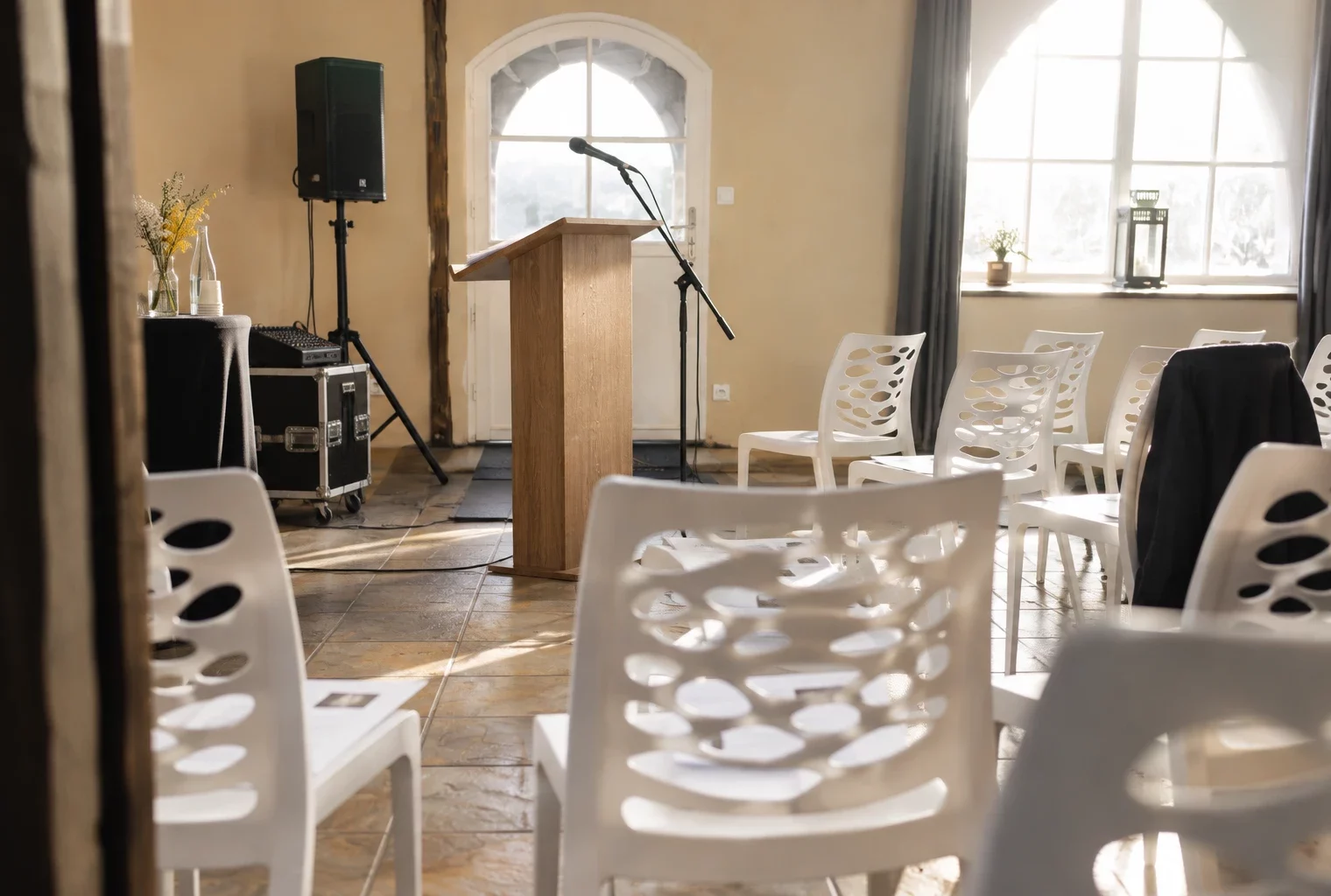 Détail d’une salle de réunion en cours d’installation, avec pied de micro, pupitre sobre et chaises sur un sol carrelé.