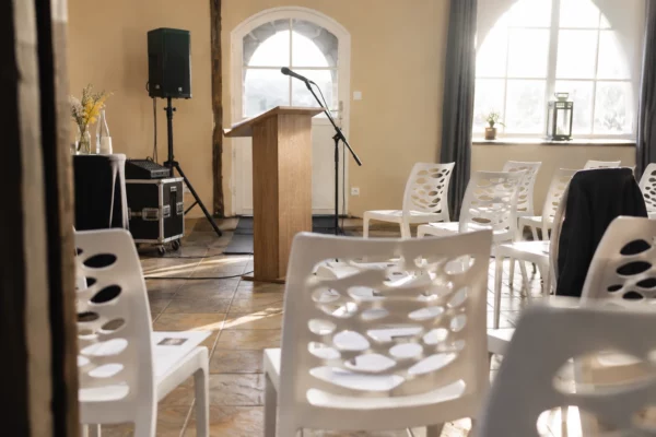 Détail d’une salle de réunion en cours d’installation, avec pied de micro, pupitre sobre et chaises sur un sol carrelé.