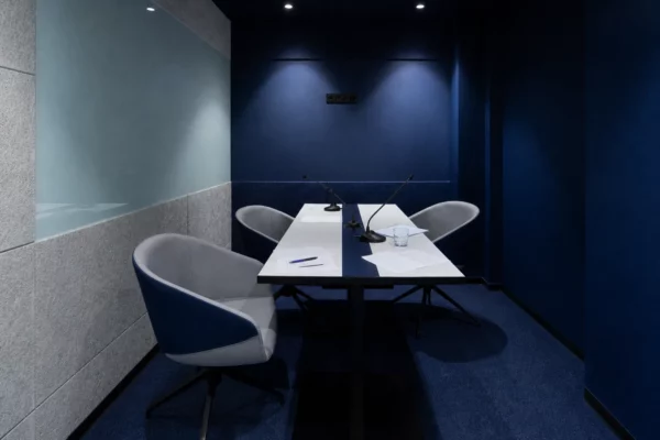 Salle de réunion bleu nuit dans un local politique, avec table centrale, micros, feuilles blanches et chaises légèrement déplacées.