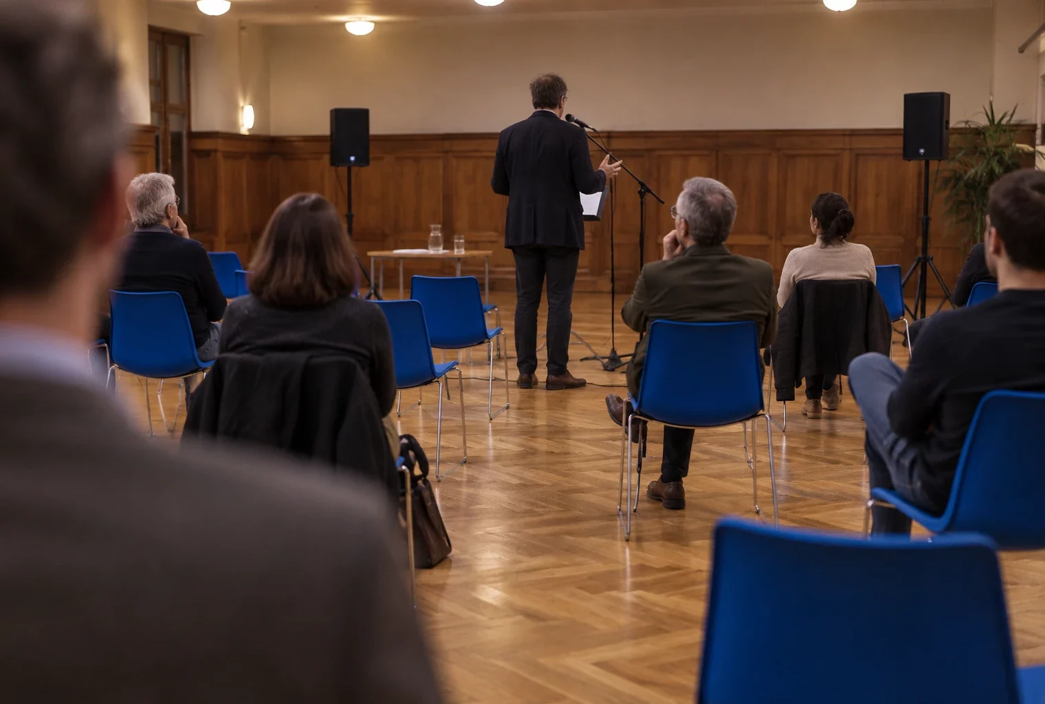 Microphone et enceintes installés devant des rangées de chaises bleues dans une salle municipale prête pour une réunion politique.