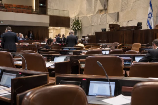 Rangées de pupitres munis de microphones dans une salle parlementaire, avec des gradins et des panneaux acoustiques au fond.