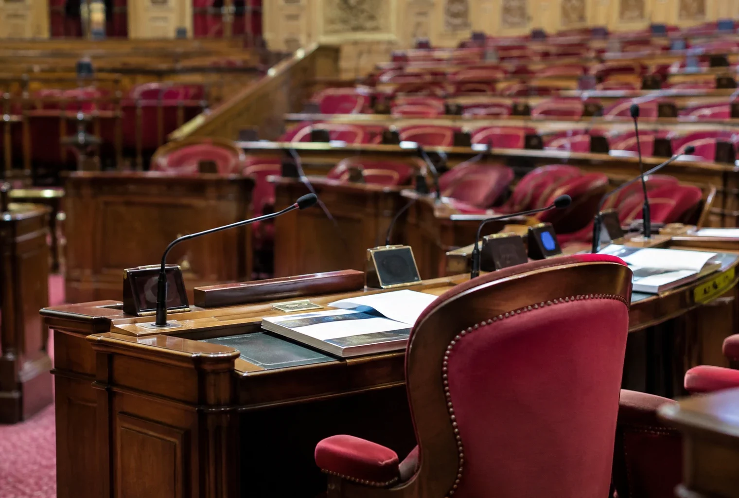 Pupitres équipés de microphones et rangées de sièges dans une salle de séance parlementaire sans occupants.