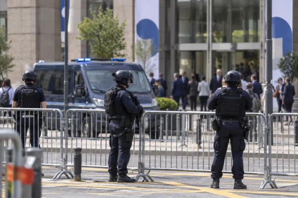 Des policiers en tenue surveillent les abords d’un lieu de congrès, derrière des barrières métalliques, avec un véhicule de police en retrait.