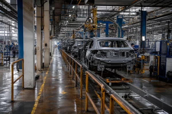 Chaîne d’assemblage Renault dans une vaste halle industrielle, carrosseries électriques, sol mouillé et lumière grise de pluie.