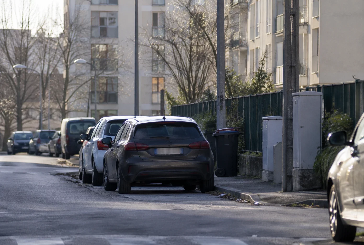 Une voiture ordinaire est garée le long d’une rue résidentielle bordée d’immeubles et d’autres véhicules stationnés.