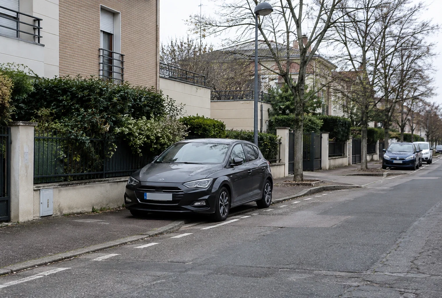 Une voiture est stationnée au bord d’une rue résidentielle, devant des façades d’immeubles et du mobilier urbain.