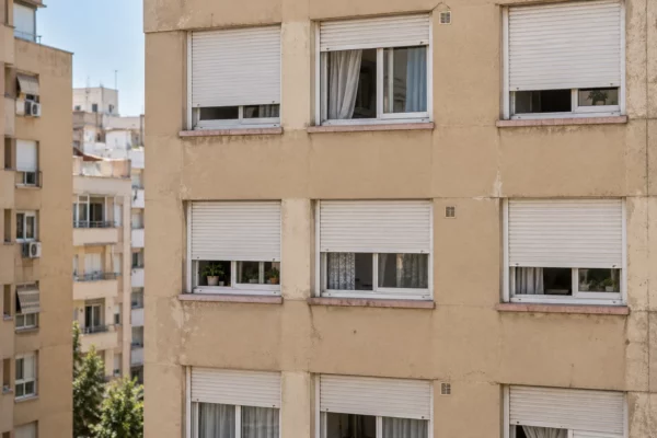 Façade d’immeuble résidentiel espagnol aux volets blancs partiellement baissés, protégeant les fenêtres de la chaleur estivale.