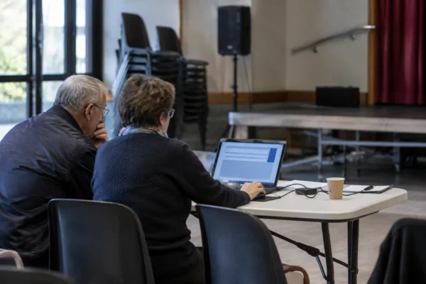 Un ordinateur portable affiche une interface de vote neutre dans une salle municipale avec des chaises empilées en arrière-plan.