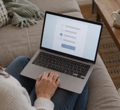 Une main posée sur le pavé tactile d’un ordinateur portable ouvert, dans un intérieur domestique sobre.