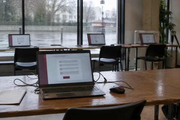 Un ordinateur portable affiche une interface de vote en ligne, avec d’autres postes informatiques installés dans la pièce.